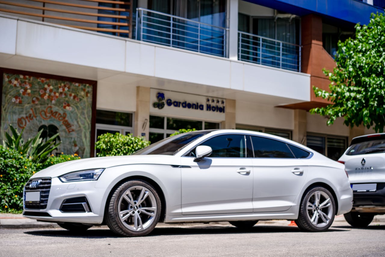 White luxury car parked in front of a hotel with modern architecture.
