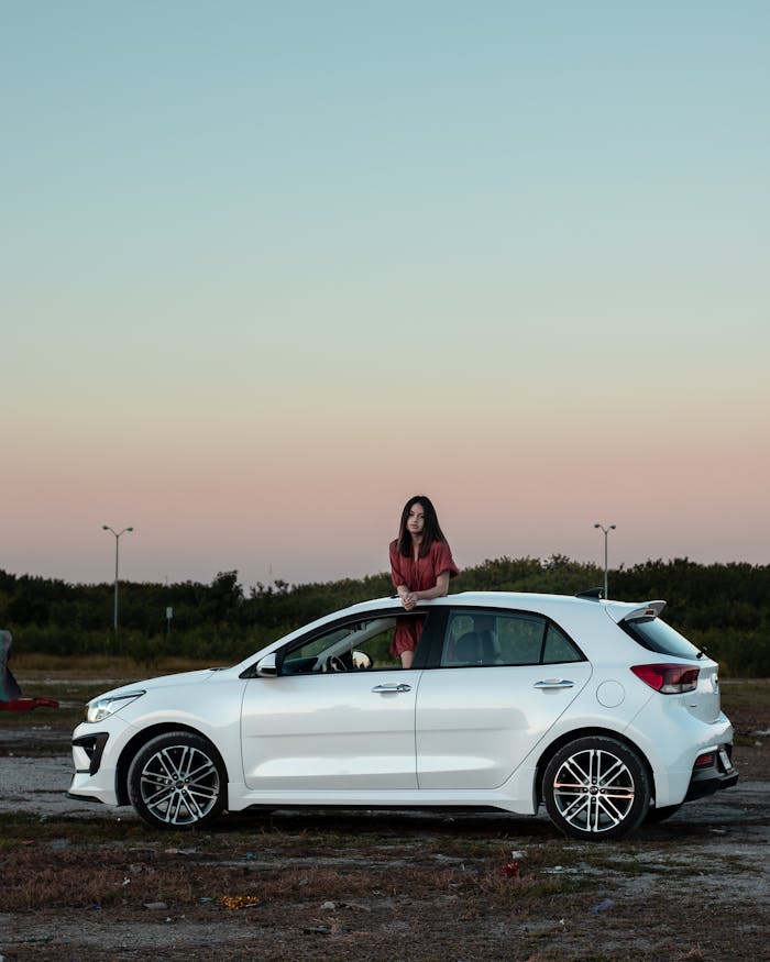 A woman stands by a white car outdoors during sunset, showcasing serene evening vibes.