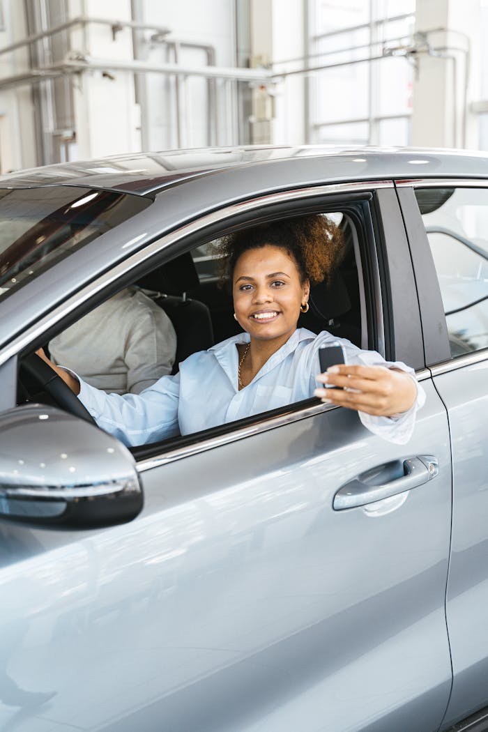 Cheerful woman with car key sitting inside a modern vehicle, showcasing joy and ownership.