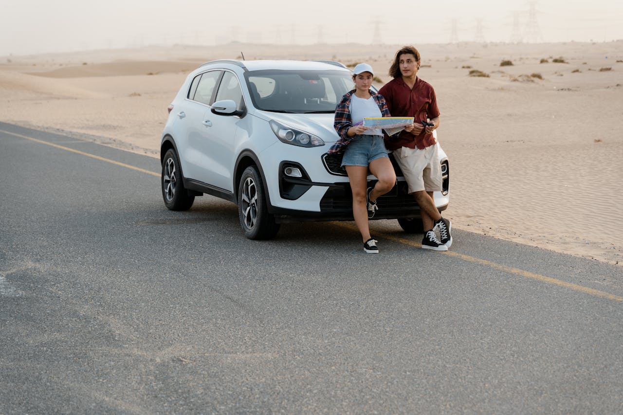 A young couple leaning on a white SUV during a road trip in the desert.